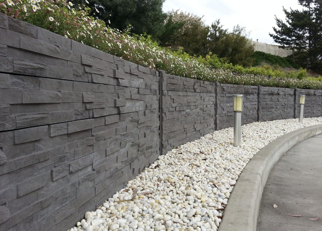 Concrete retaining wall with stacked stone texture alongside white gravel landscaping in Tacoma, WA
